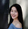 Person with long dark hair smiling in front of a light-colored wall.